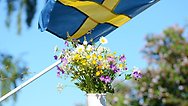 Blommor i vit vas och en svensk flagga fladdrar i vinden.