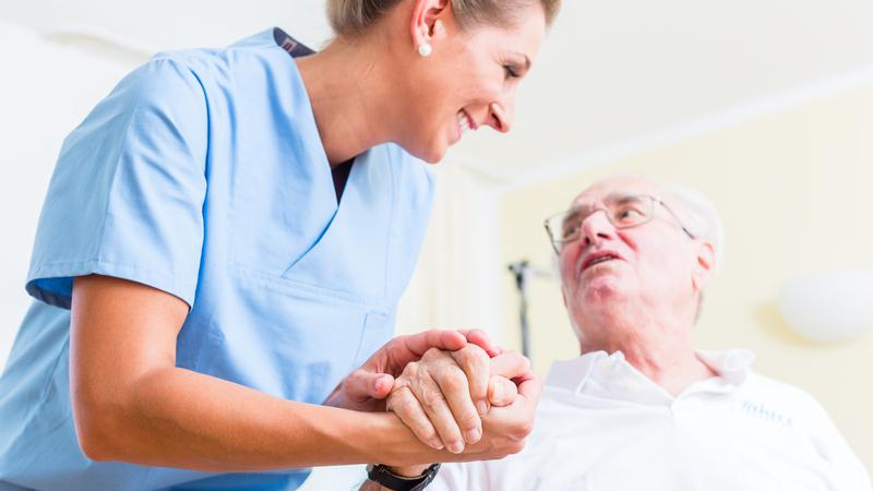 Sköterska håller en äldre mans hand.
