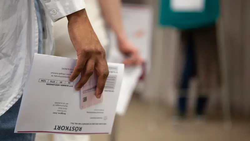 En hand håller i ett röstkort och i en legitimation. 