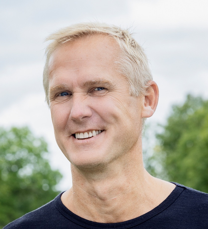 En man i svart skjorta ler mot kameran.