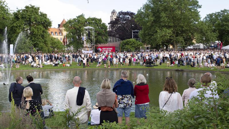 Människor står vid Almedalens damm och lyssnar på politikertal.