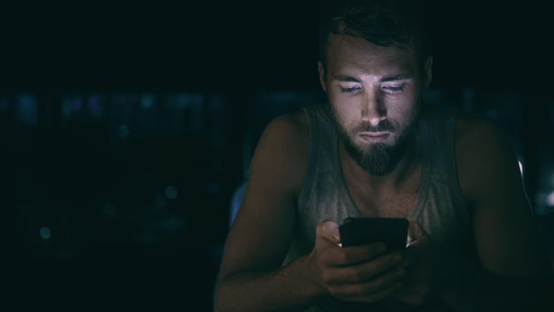 En man som tittar på sin mobiltelefon i mörkret.