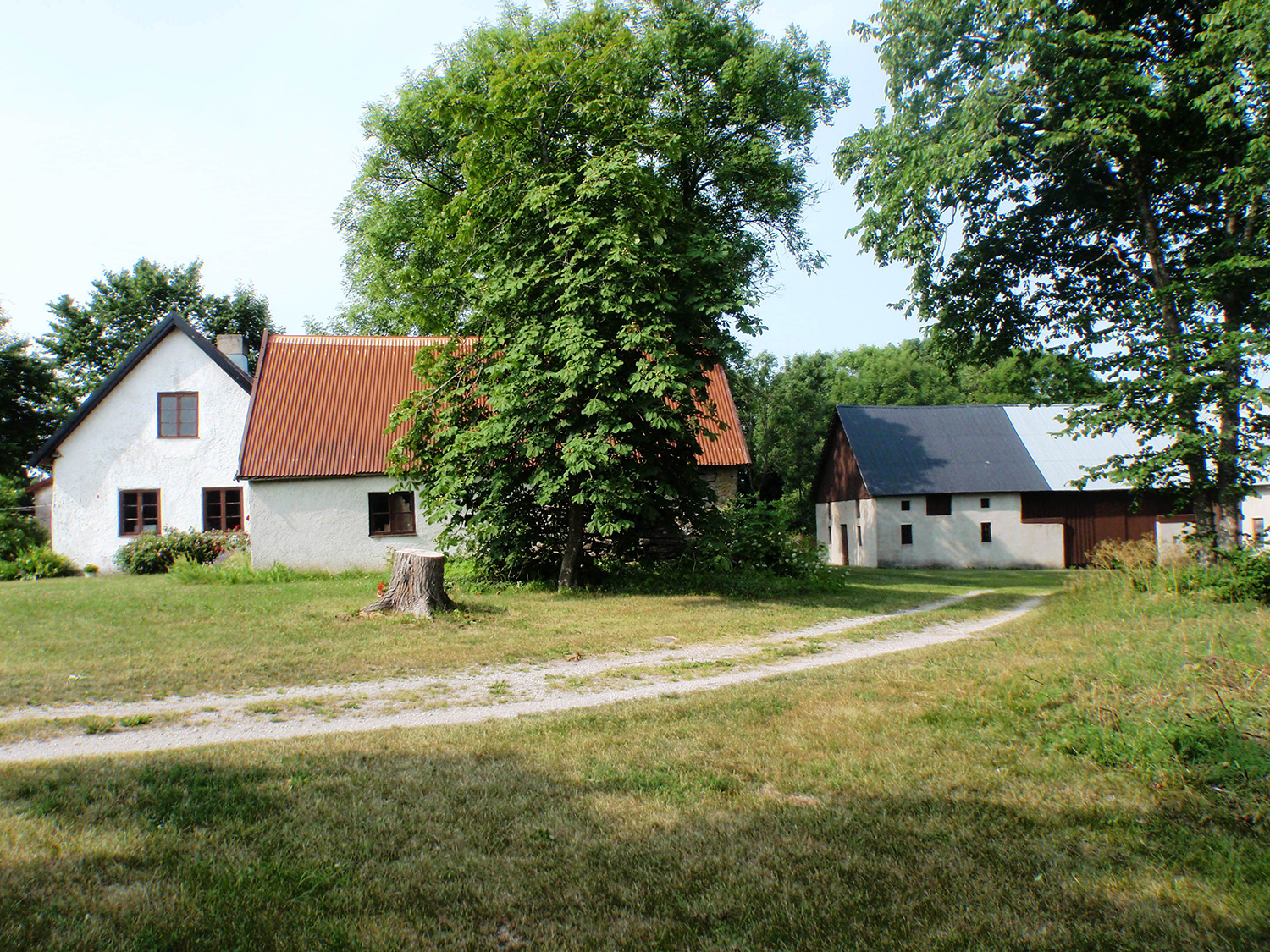 Två vita hus med bruna fönster och bruna plåttak. På gården finns även en vit lada.