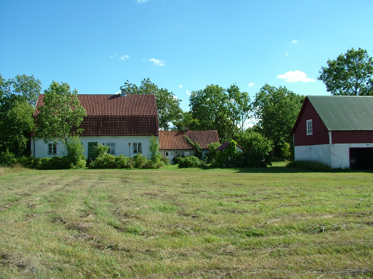 Två vita hus med bruna tegeltak och en rödvit lada med ett plåttak.