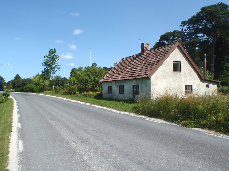 Ett litet vitt hus ligger längs en bilväg.