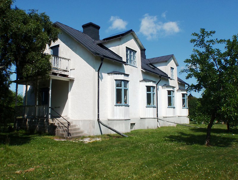 Ett vitt hus med blåa fönster, svart plåttak och välskött gräsmatta.