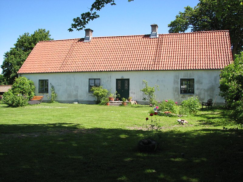 Ett vitt hus med gröna fönster, grön ytterdörr och ett rött tak med två skorstenar.
