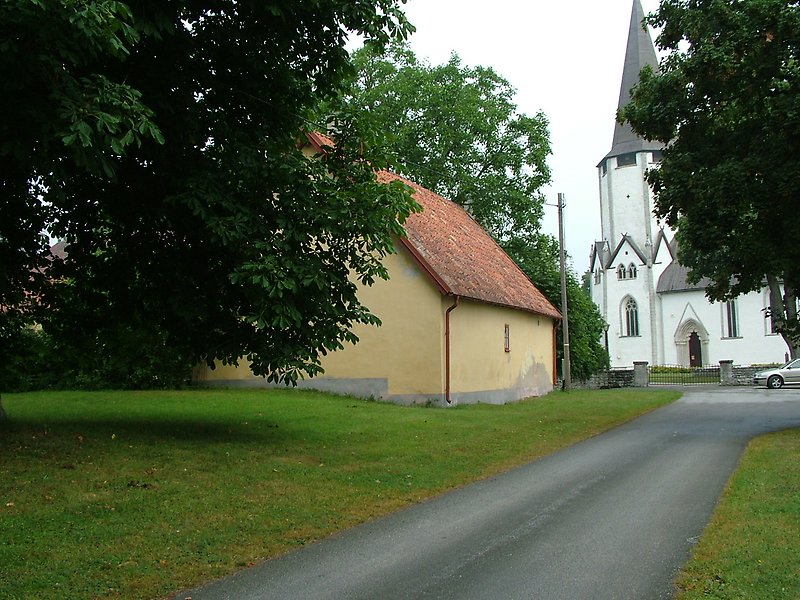 På vänster sida av vägen ligger ett gult hus, och längre bort finns det en vit kyrka.