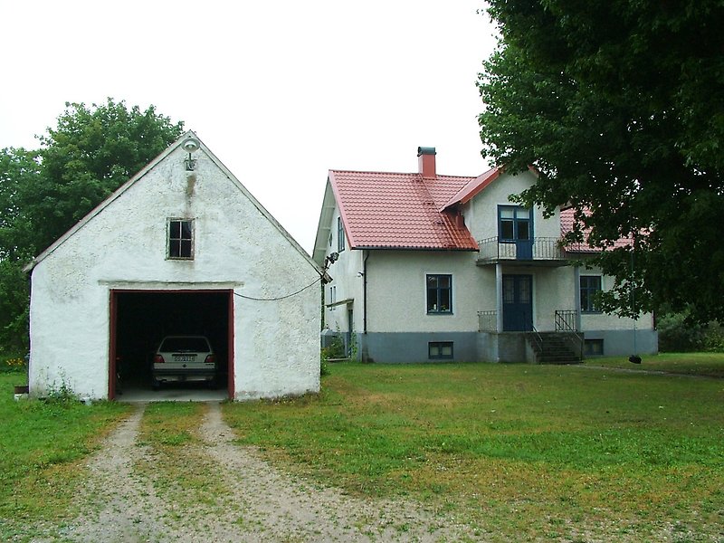 Ett vitt hus med rött tak, ett garage med parkerad bil.