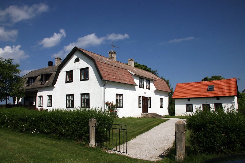 Ett vitt hus med svarta fönster, ett rött tak och en svart ytterdörr.