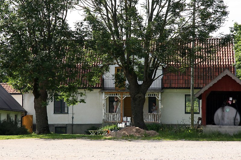 Ett vitt hus med gröna fönster, bruna dörrar och ett rött tegeltak.