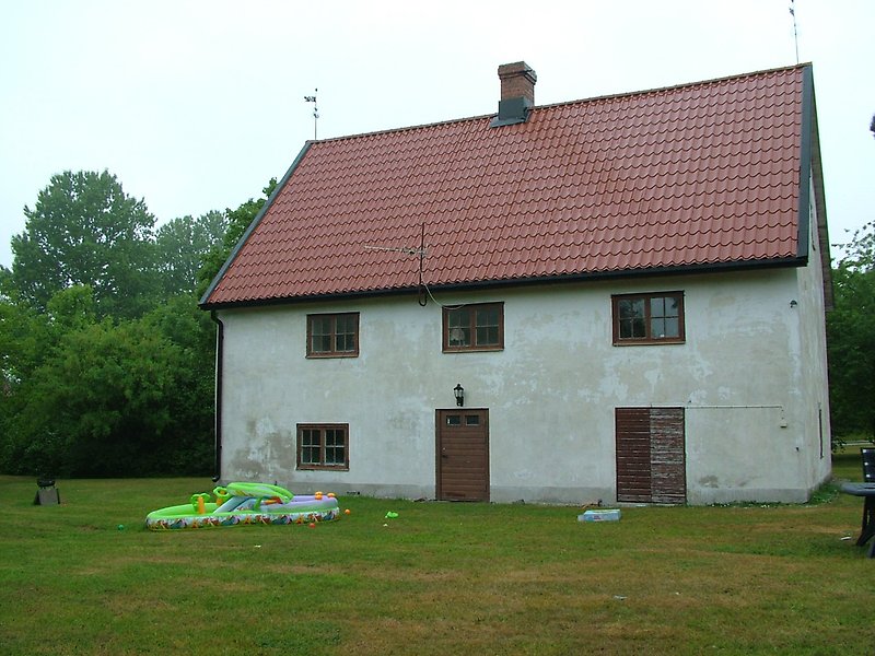 Ett vitt hus med bruna dörrar, bruna fönster och ett rött tak med en skorsten.