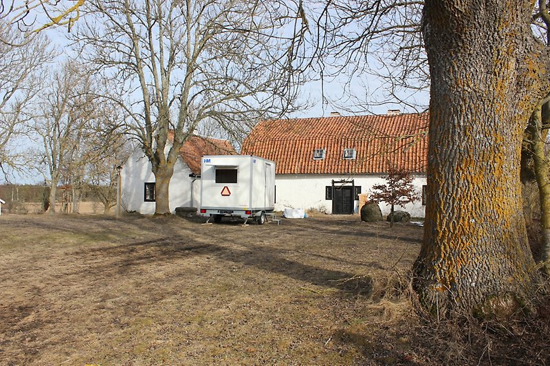 Två vita byggnader med orange tak, svarta dörrar, svarta fönster och ett vitt hästsläp parkerad på gården.