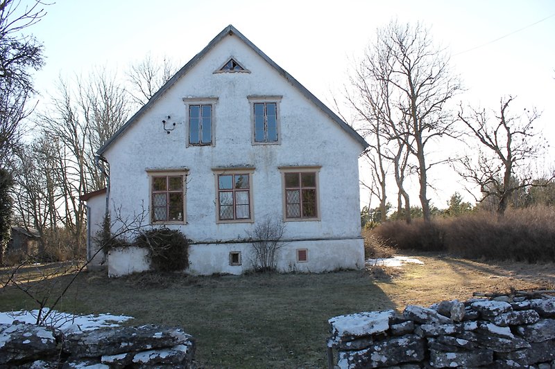 Gaveln på ett vitt hus med bruna fönster och en stenmur på gården.