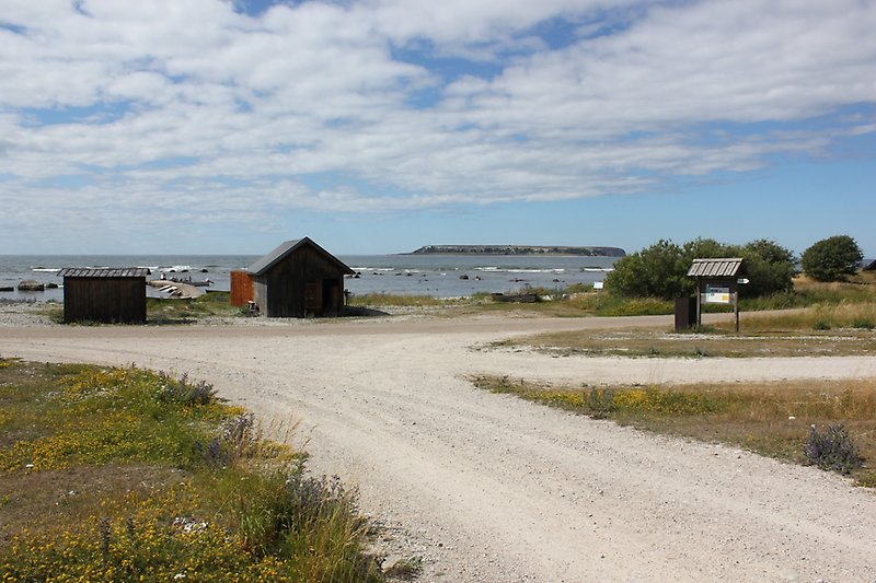 Två svarta bodar är placerade längs grusvägen i närheten av vattnet med utsikt över Stora Karlsö.