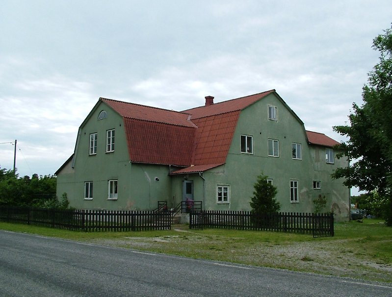 En stor tvåvåningsbyggnad med gröna väggar, vita fönster och ett rött tak.