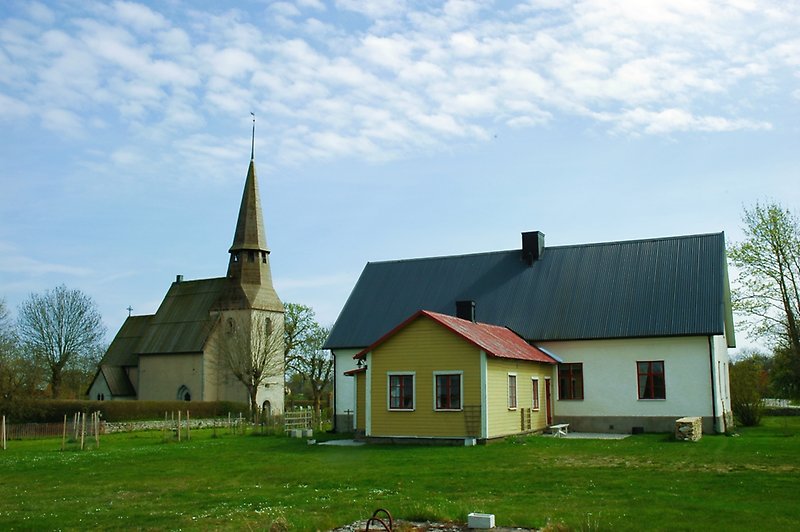 Höger om Andres kyrka finns det ett vitt hus med röda fönster och ett svart plåttak.