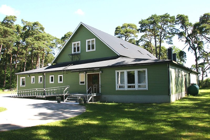 En grön bygdegård med en träfasad, vita fönster och ett svart tak.