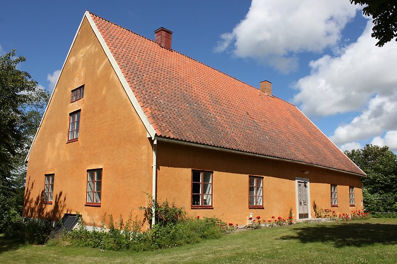 Ett orange hus med röda fönster och ett rött tegeltak med en skorsten.