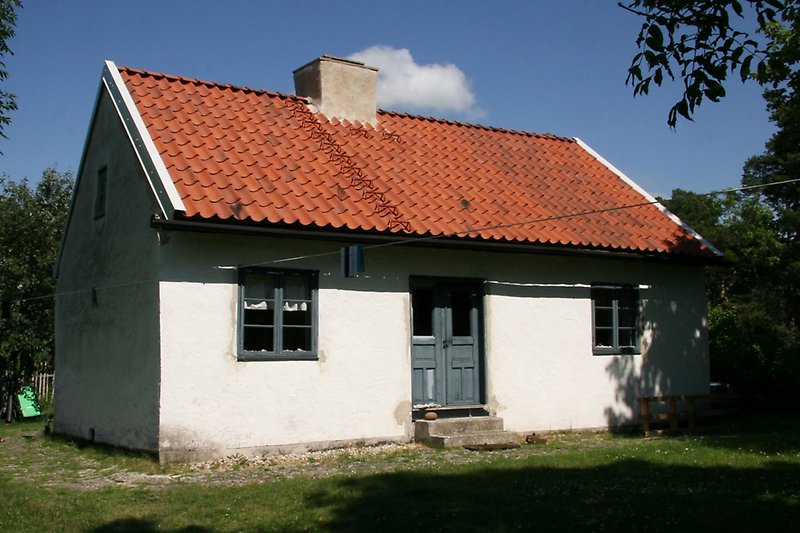 Ett litet vitt hus med blåa fönster och ett rött tegeltak med en skorsten.