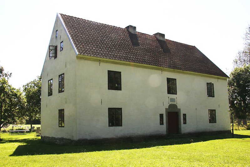 Ett tvåvånings gårdshus med svarta fönster, svarta dörrar och ett rött tegeltak.
