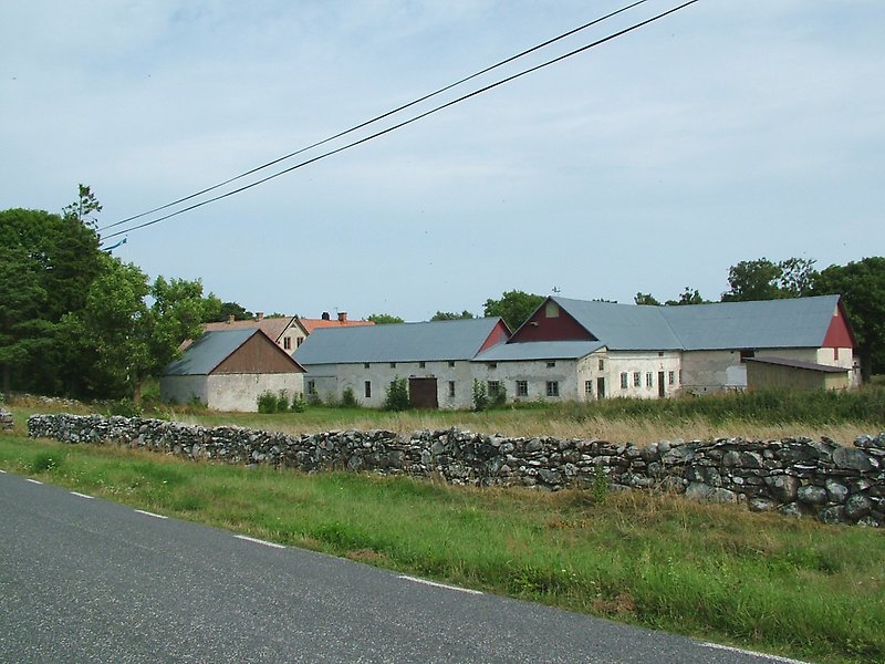 På höger sida av vägen, i närheten av en stenmur, finns det ett antal gårdsbyggnader.
