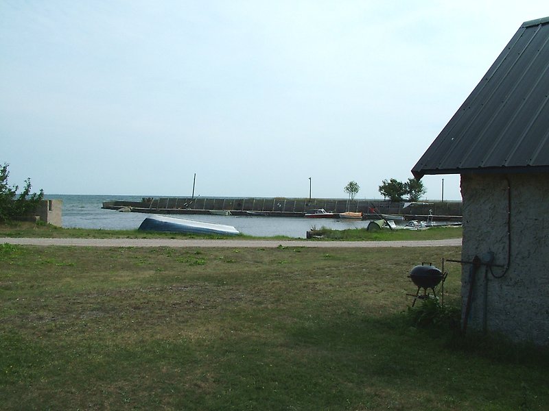 Bredvid en fiskebod står det en grill, längre bort vid hamnen ser man flera parkerade småbåtar.
