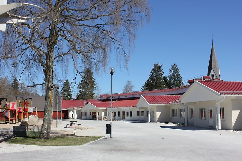 En skolgård och en vit skolbyggnad med vita fönster och ett rött plåttak.