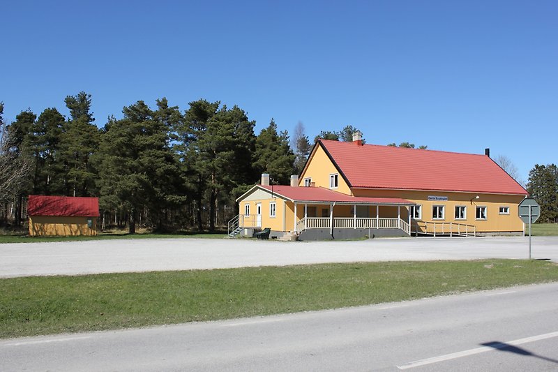 En gul bygdegård med vita fönster och ett rött tak som ligger längs vägen.