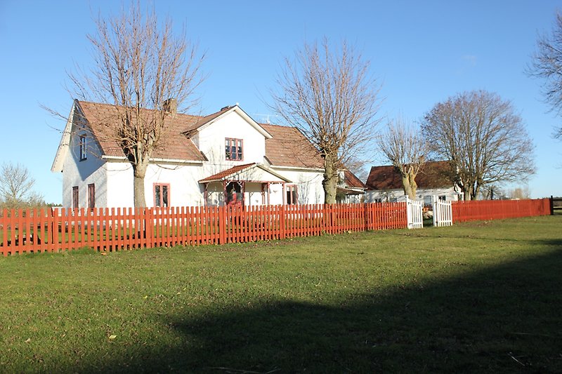 Ett vitt hus med röda fönster, rött tak och rött staket.