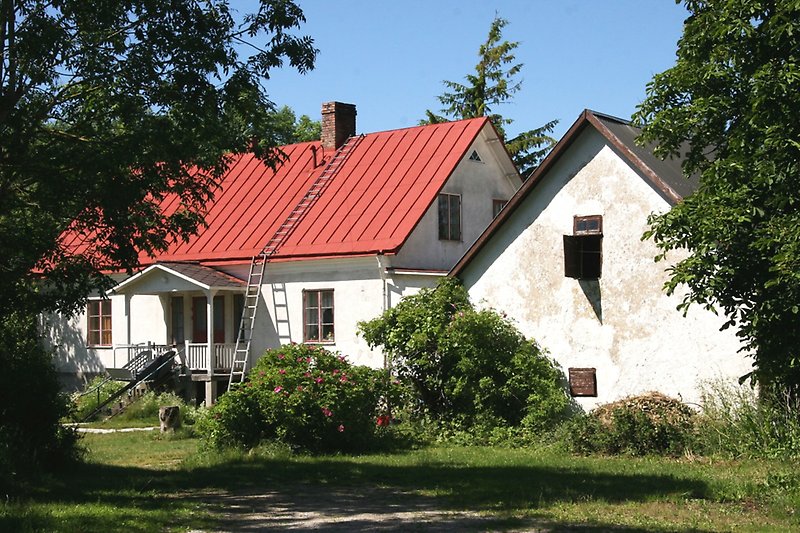 Vitt hus med rött tak och en gårdshus under sommartid