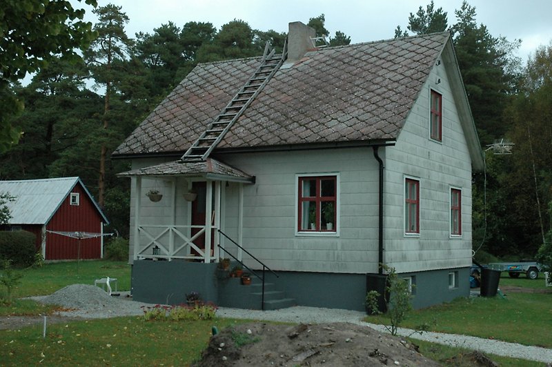 Ett litet grå hus med bruna fönster och en brun ytterdörr.
