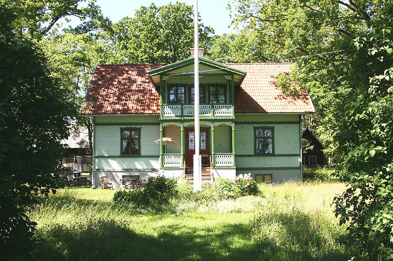 Ett olivgrönt hus med en träfasad, bruna fönster, bruna dörrar och ett rött tak.