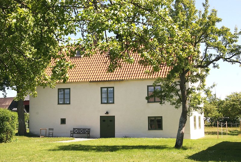 Ett vitt hus med gröna fönster, ett orange tak och en grön ytterdörr.