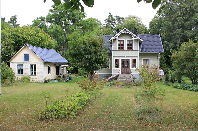 Ett olivgrönt hus med träfasad, bruna fönster och ett svart plåttak.