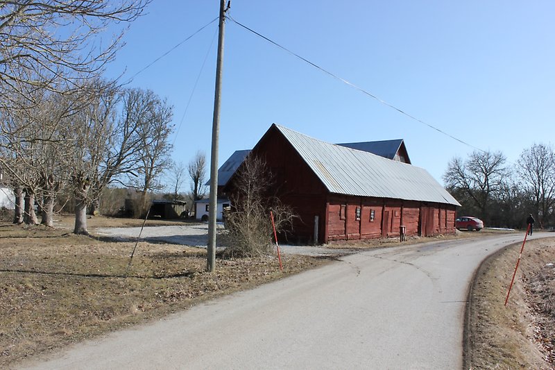 En röd ladugård med grå plåttak ligger längs vägen.