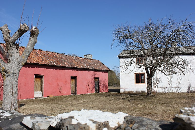 Ett vitt hus med bruna fönster och ett rosa gårdshus med ett rött tak.