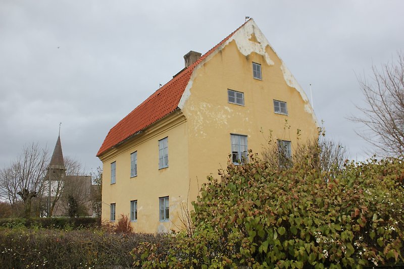 Ett gult hus med gråa fönster och ett rött tak.