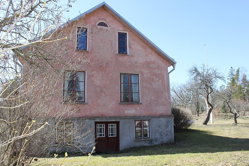 Gaveln på ett rosa hus med mörkröda fönster med vita detaljer.
