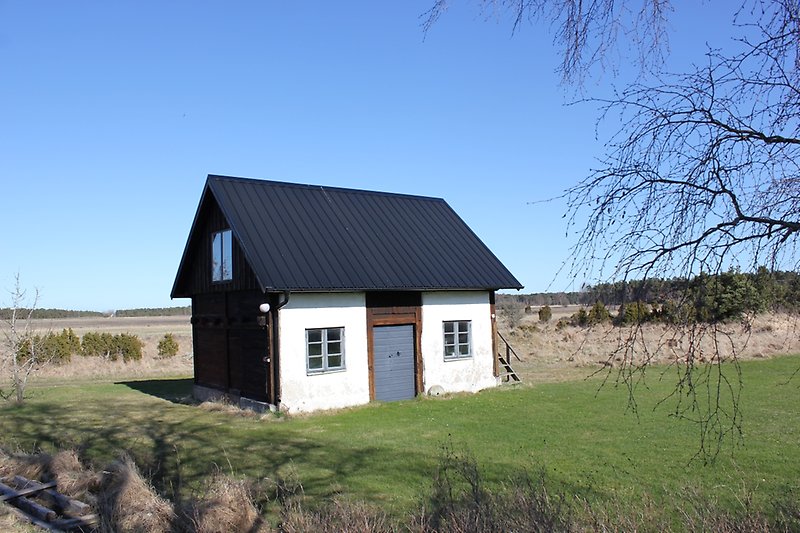 En liten ensamstående stuga med blåa fönster och ett svart tak.