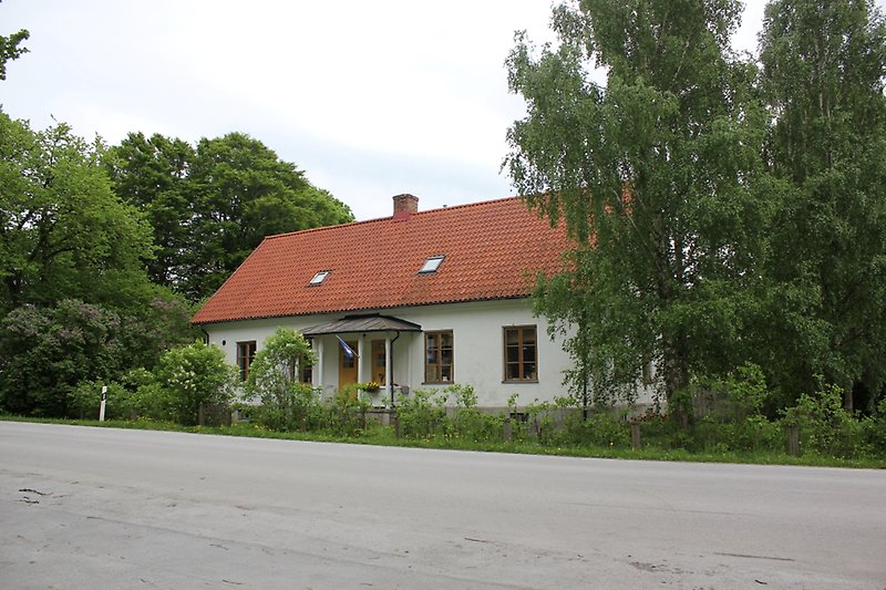 Ett vitt hus som ligger längs vägen har bruna fönster och ett rött tak.