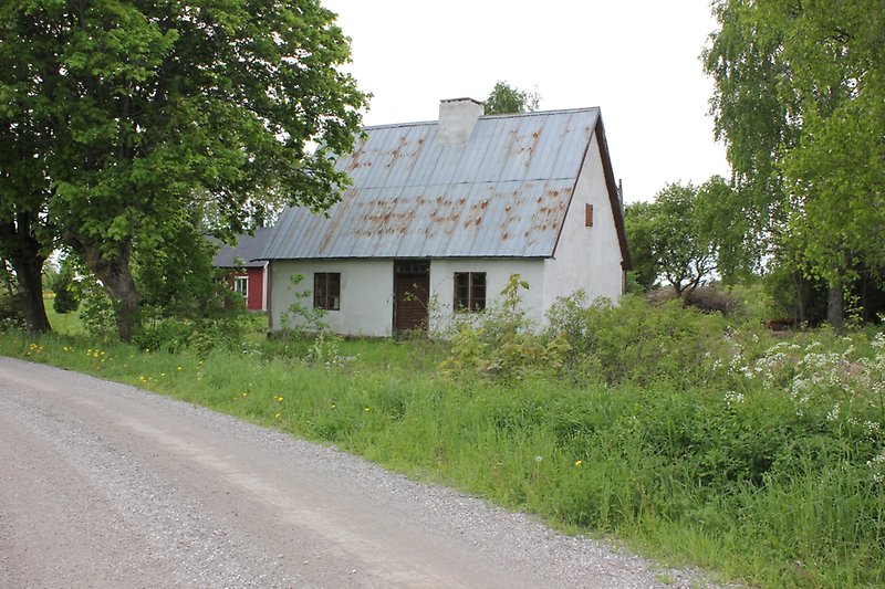 Ett litet vitt hus med bruna fönster, ett plåttak med en skorsten och en brun ytterdörr.