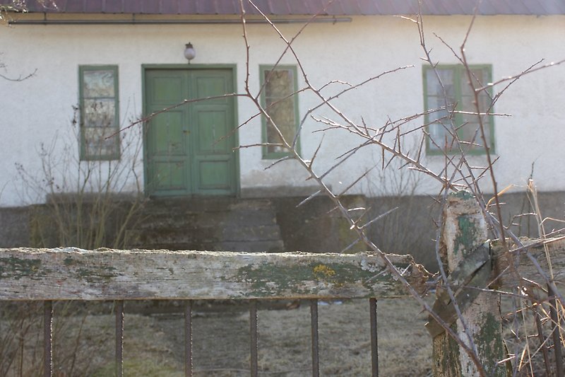 Bakom grinden finns det ett vitt hus med gröna fönster och en grön ytterdörr.
