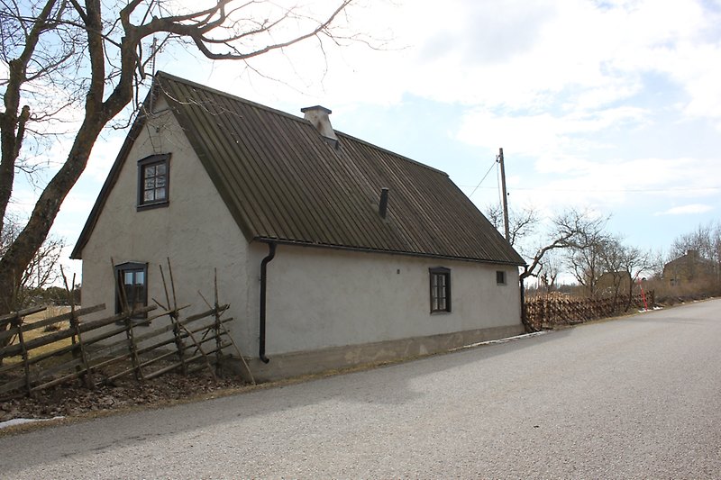 Ett vitt hus som ligger längs vägen har gråa fönster och ett trätak med en skorsten.