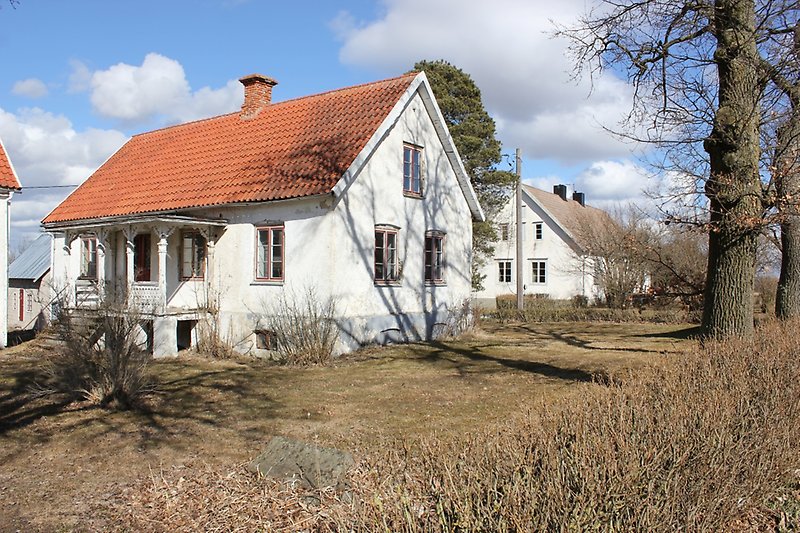 Ett vitt hus med bruna fönster, en brun ytterdörr och ett rött tegeltak med en skorsten.