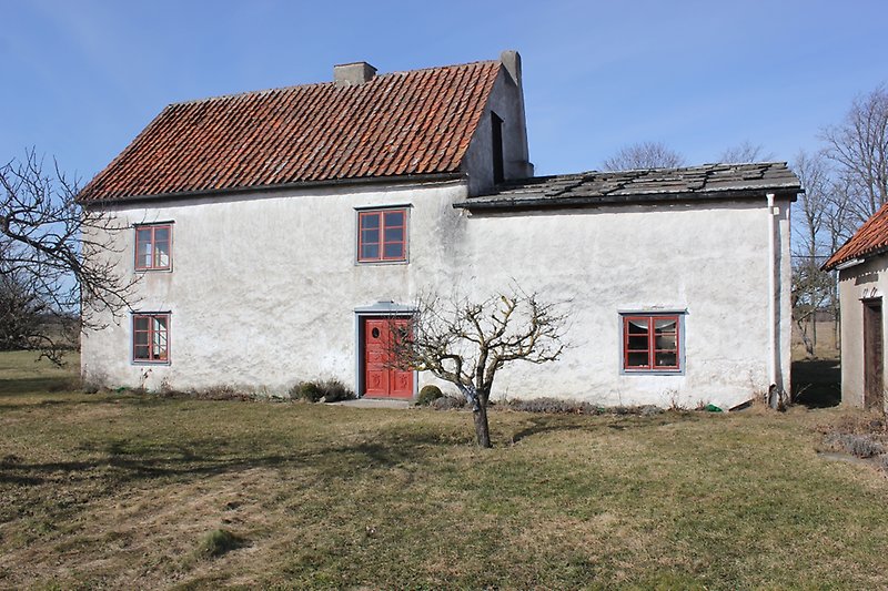 Ett litet hus med putsade väggar, röd ytterdörr, röda fönster och ett orange tak.