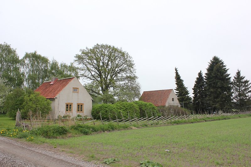 Två gråa hus med röda tak på landsbygden.