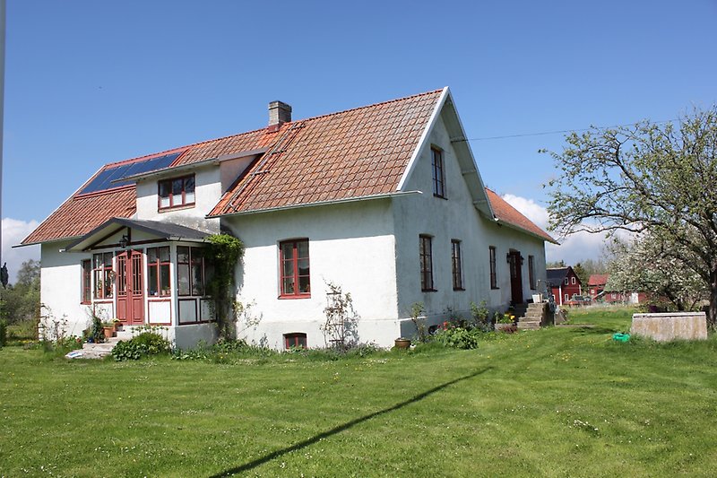 Ett vitt hus av två våningar, röda dörrar och fönster samt solpaneler på taket.
