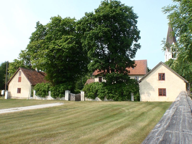 Bakom den nyklippta gräsmattan finns flera byggnader, och längst bort syns en vit kyrka.