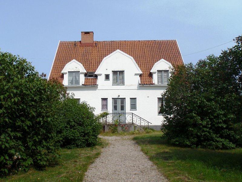Ett vackert vitt hus bestående av två våningar med gråa fönster, grå ytterdörr och ett rött tak.